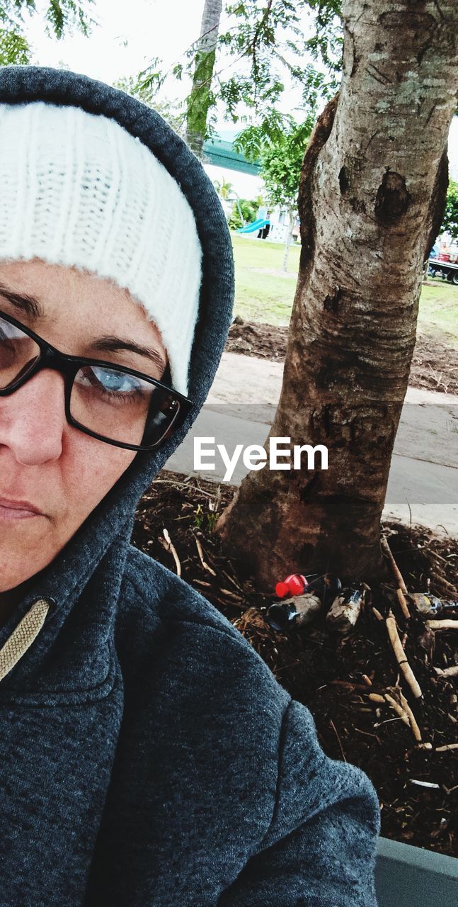 one person, glasses, tree, adult, portrait, leisure activity, spring, lifestyles, eyeglasses, day, tree trunk, trunk, nature, men, headshot, clothing, outdoors, plant, hat, front view, women, casual clothing, looking at camera, person, young adult, close-up, human face, blue, winter, female