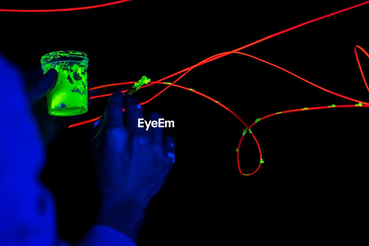 Midsection of hand holding illuminated lights against black background