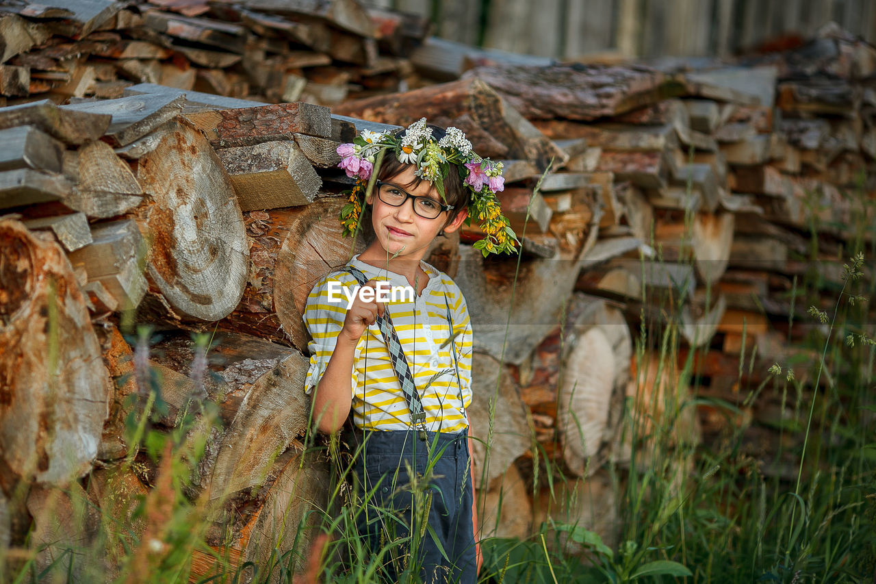 Portrait of girl standing by woodpile outdoors