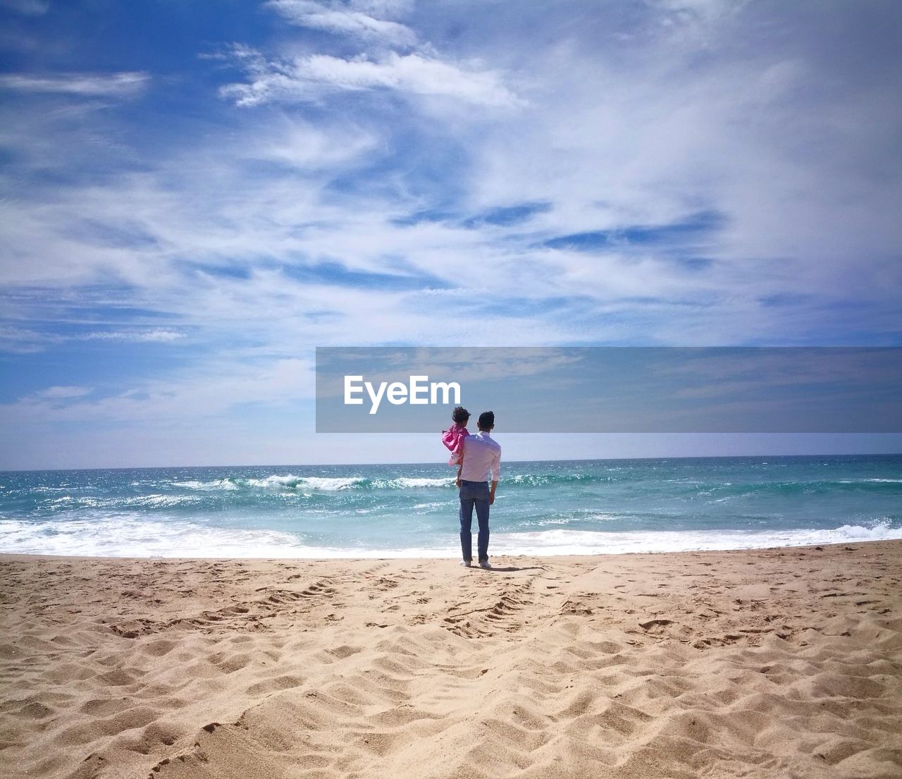 Rear view of father and daughter standing on beach against sky