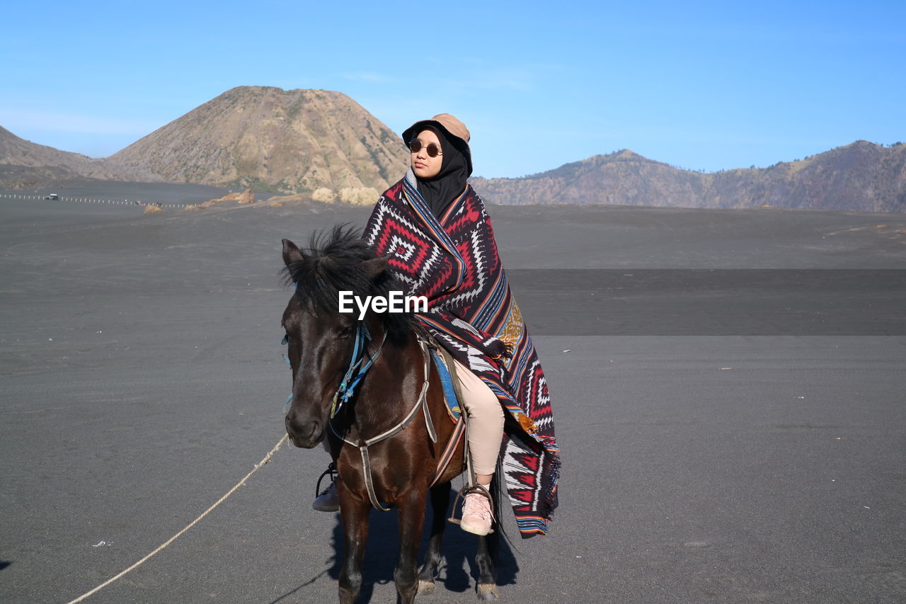Woman riding horse at desert against sky