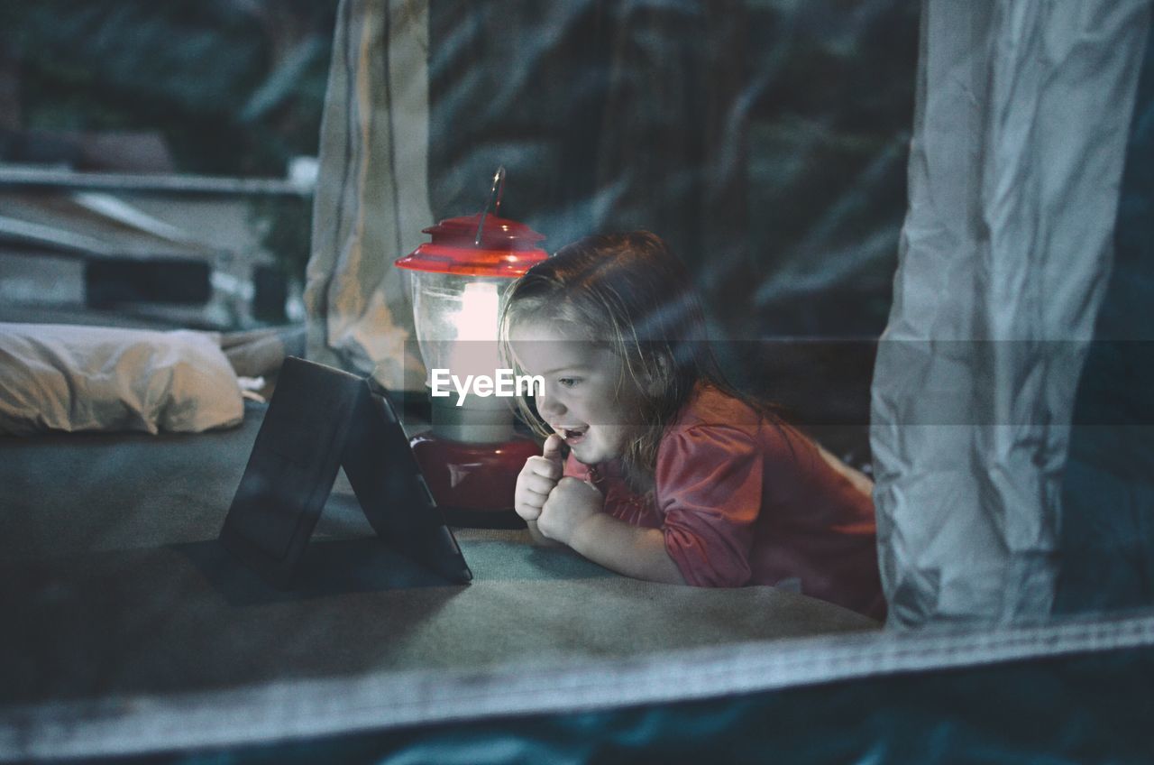 Girl looking at digital tablet by illuminated lantern on bed at home