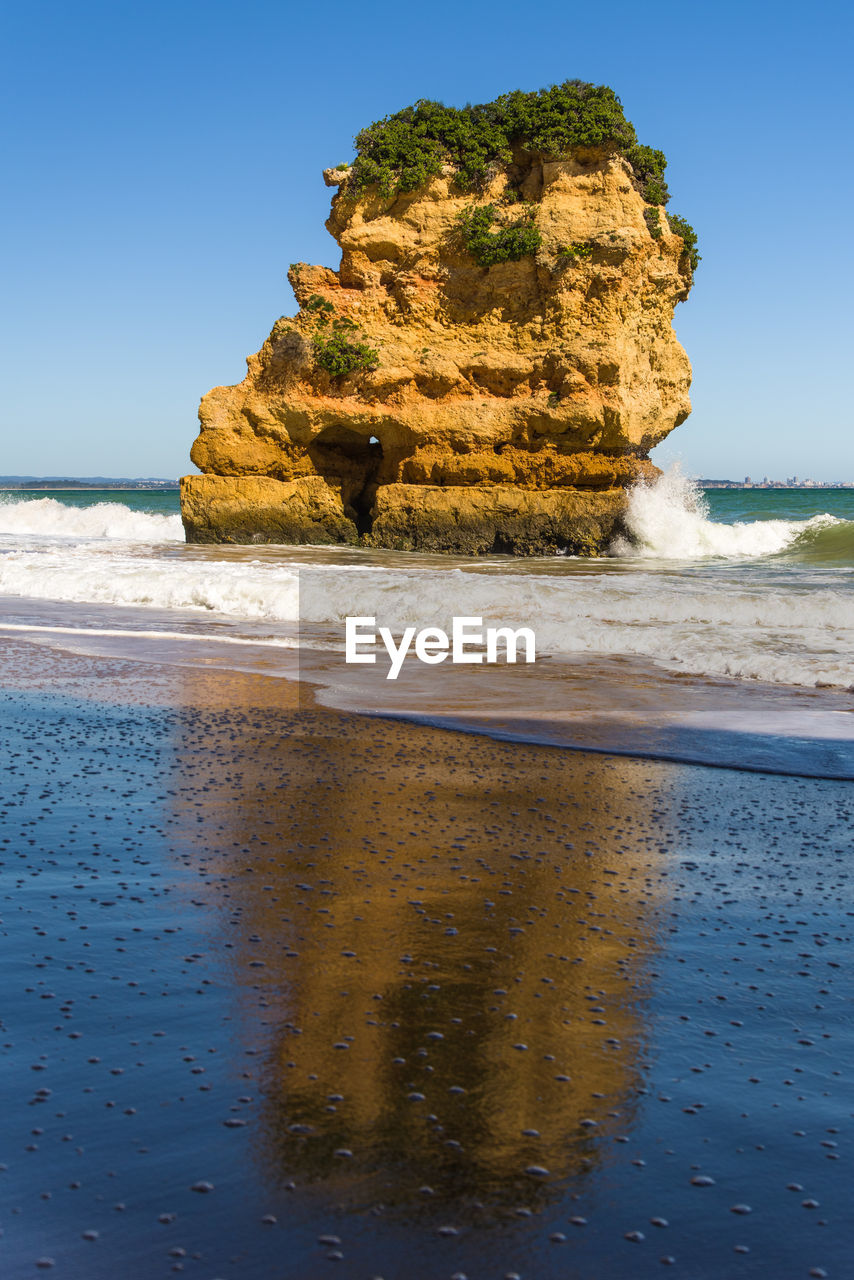 Rock formation on beach against sky with reflection 