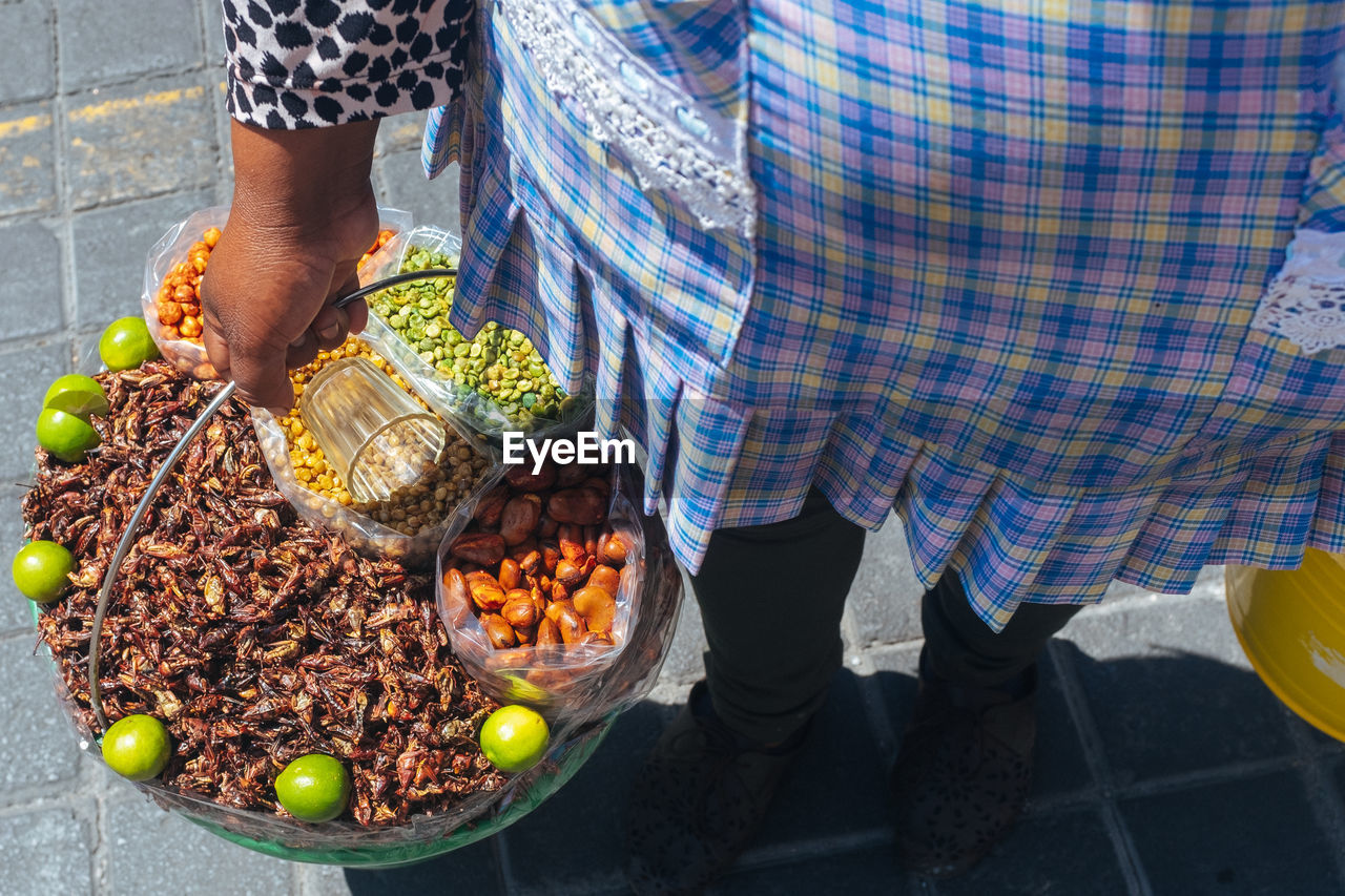 Low section of woman carrying food in buckets on street