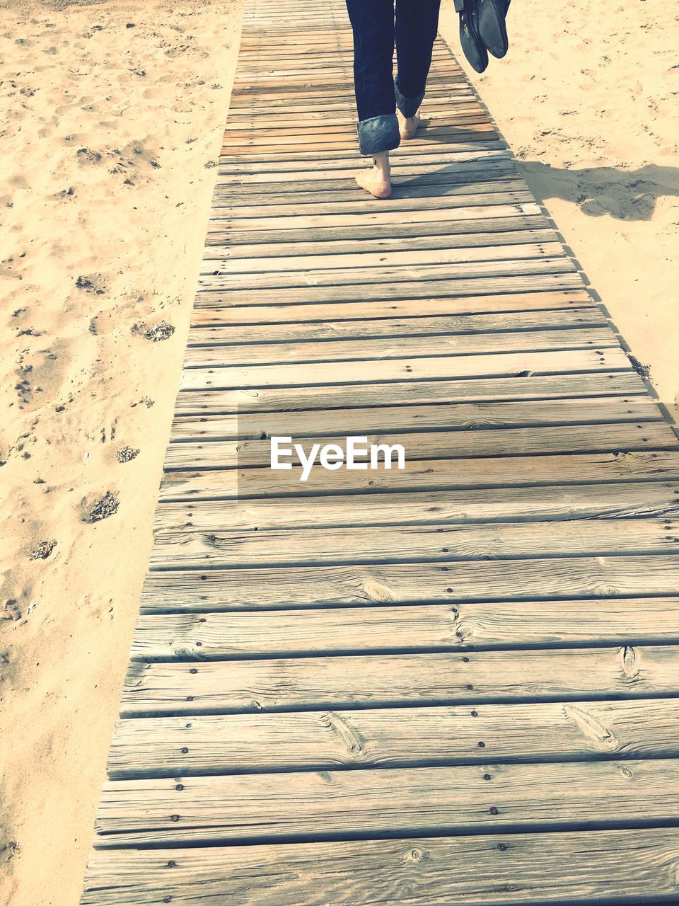 Low section of man walking on boardwalk at beach