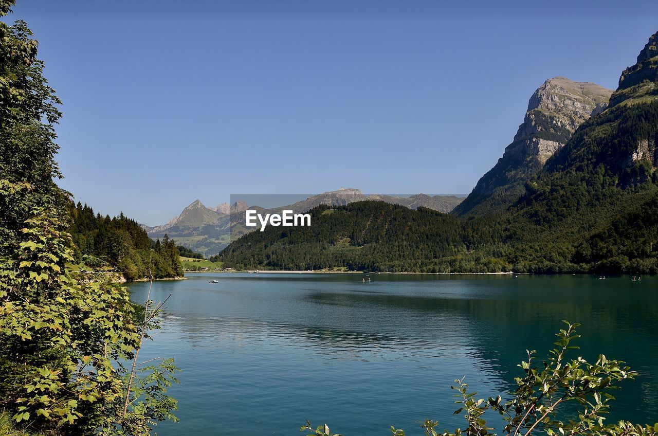 Scenic view of lake and mountains against clear blue sky