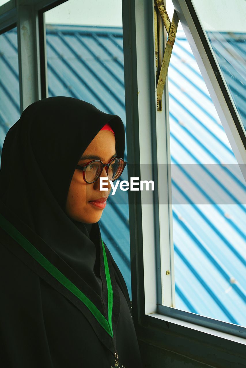 Mid adult woman in hijab looking through window while standing at home