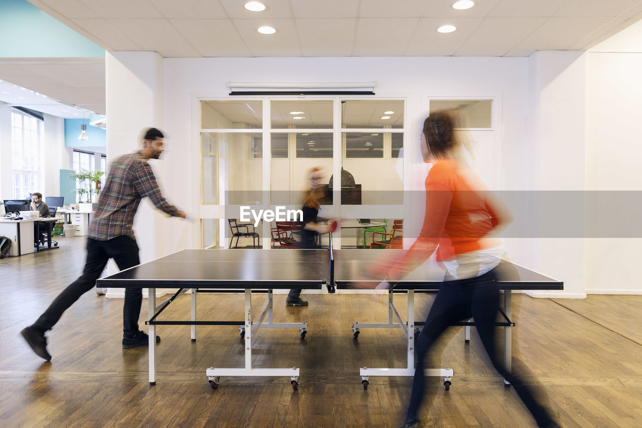 Blurred motion of business people playing table tennis in creative office