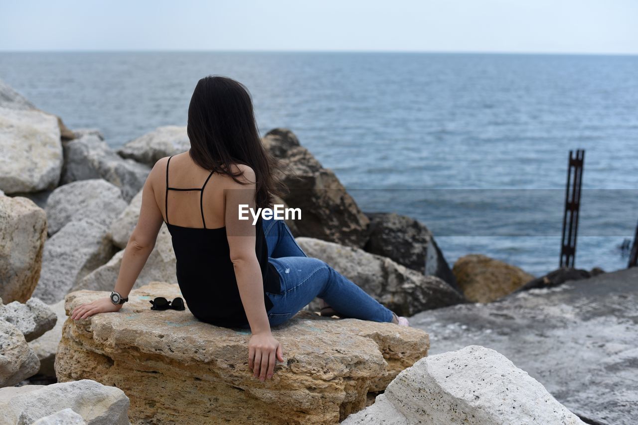 Rear view of woman sitting on rock by sea