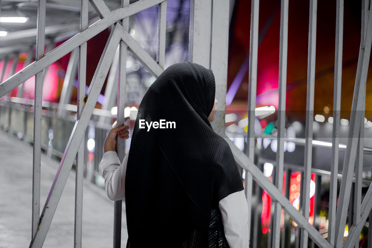 Rear view of woman in hijab standing by gate