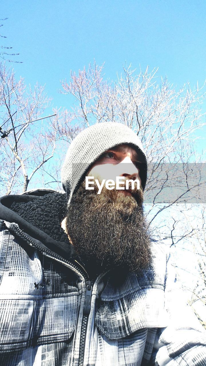 Low angle view of mid adult man looking away while standing against clear sky