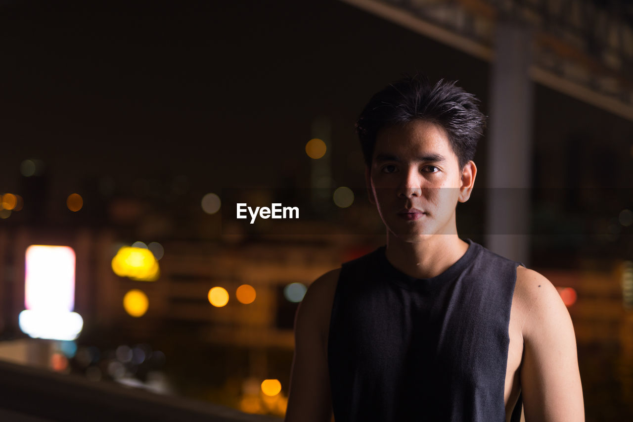 PORTRAIT OF YOUNG MAN STANDING AT NIGHT