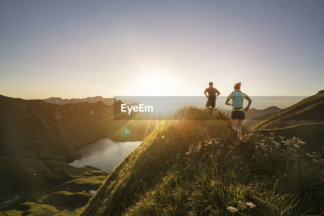 Germany, allgaeu alps, man and woman running on mountain trail