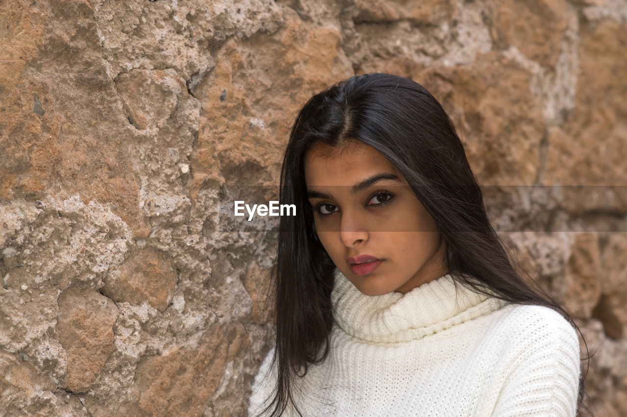 PORTRAIT OF YOUNG WOMAN AGAINST WALL