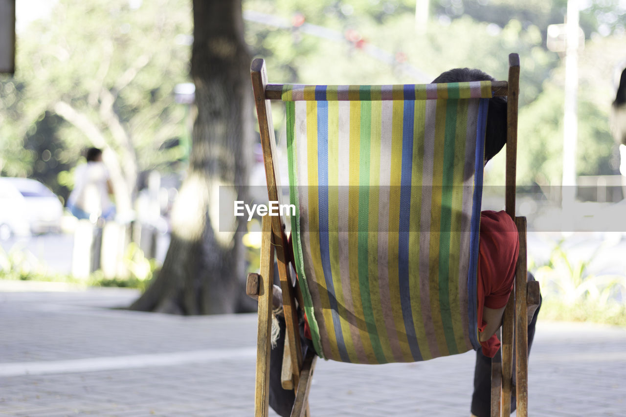 Rear view of man sitting on deck chair at footpath