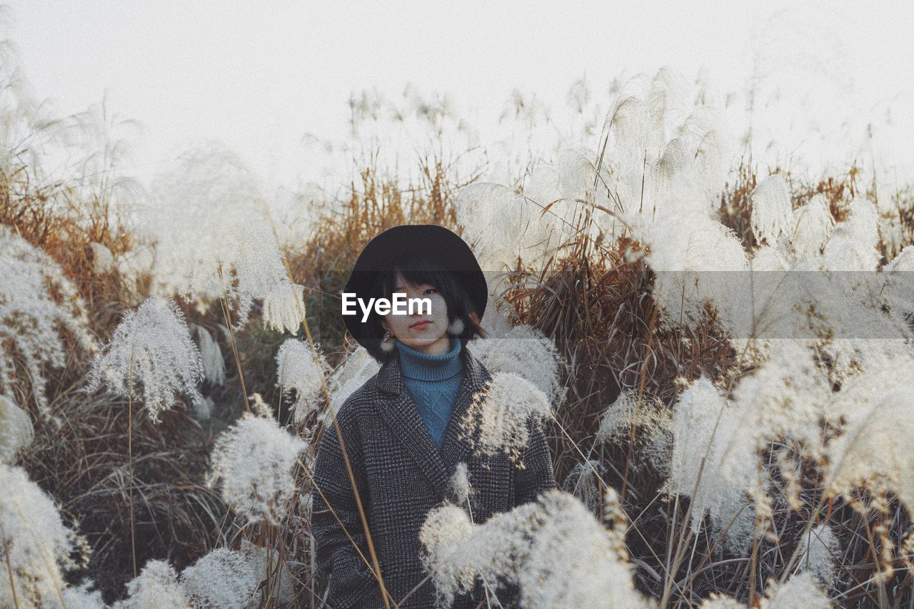 PORTRAIT OF WOMAN STANDING BY SNOW COVERED PLANTS