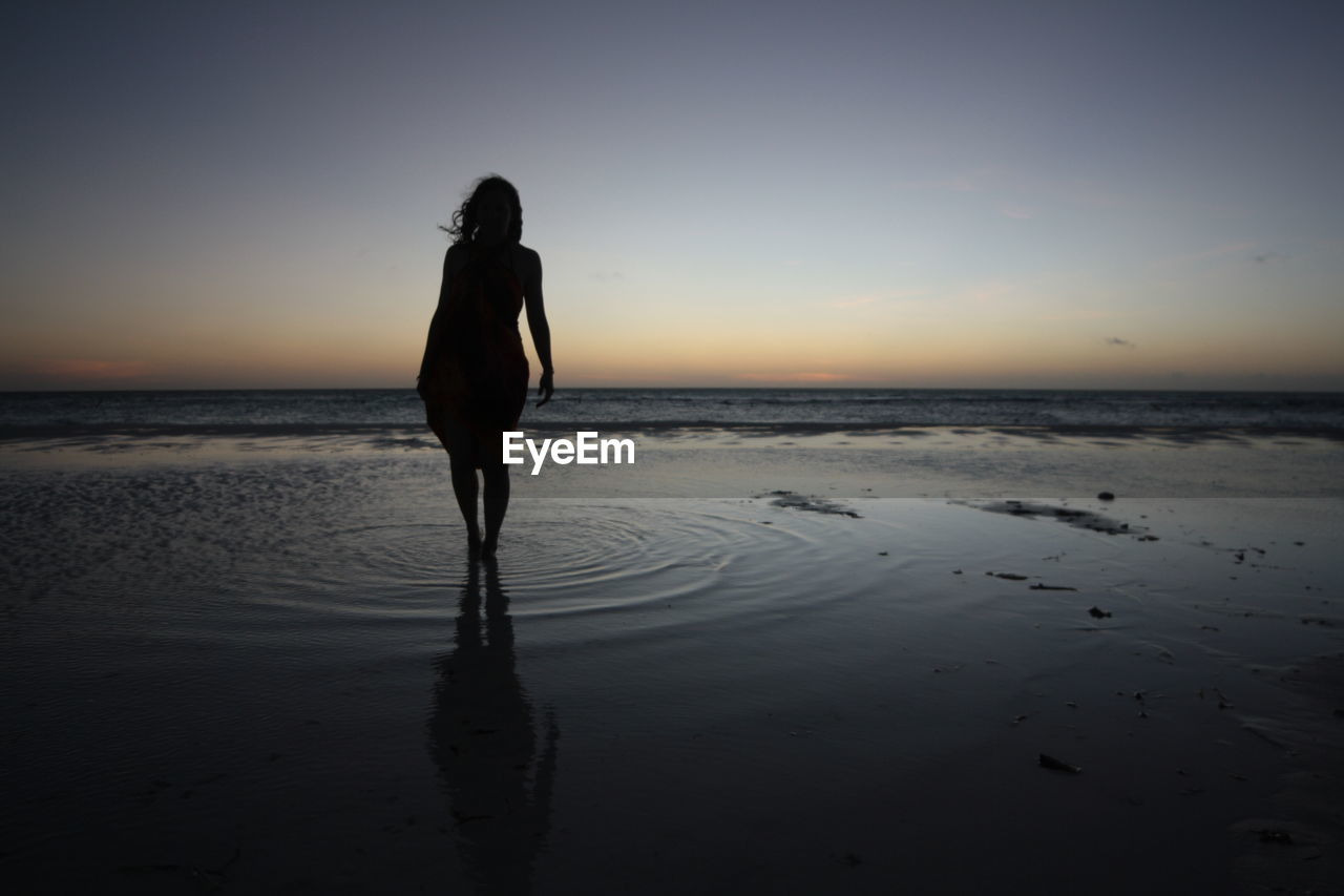 Full length of silhouette woman standing at beach against sky during sunset