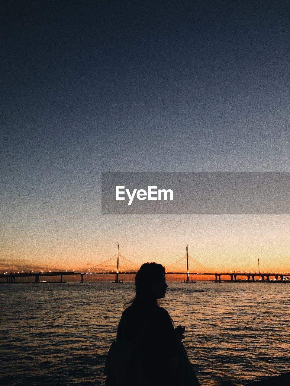 Rear view of silhouette person on suspension bridge against sky during sunset