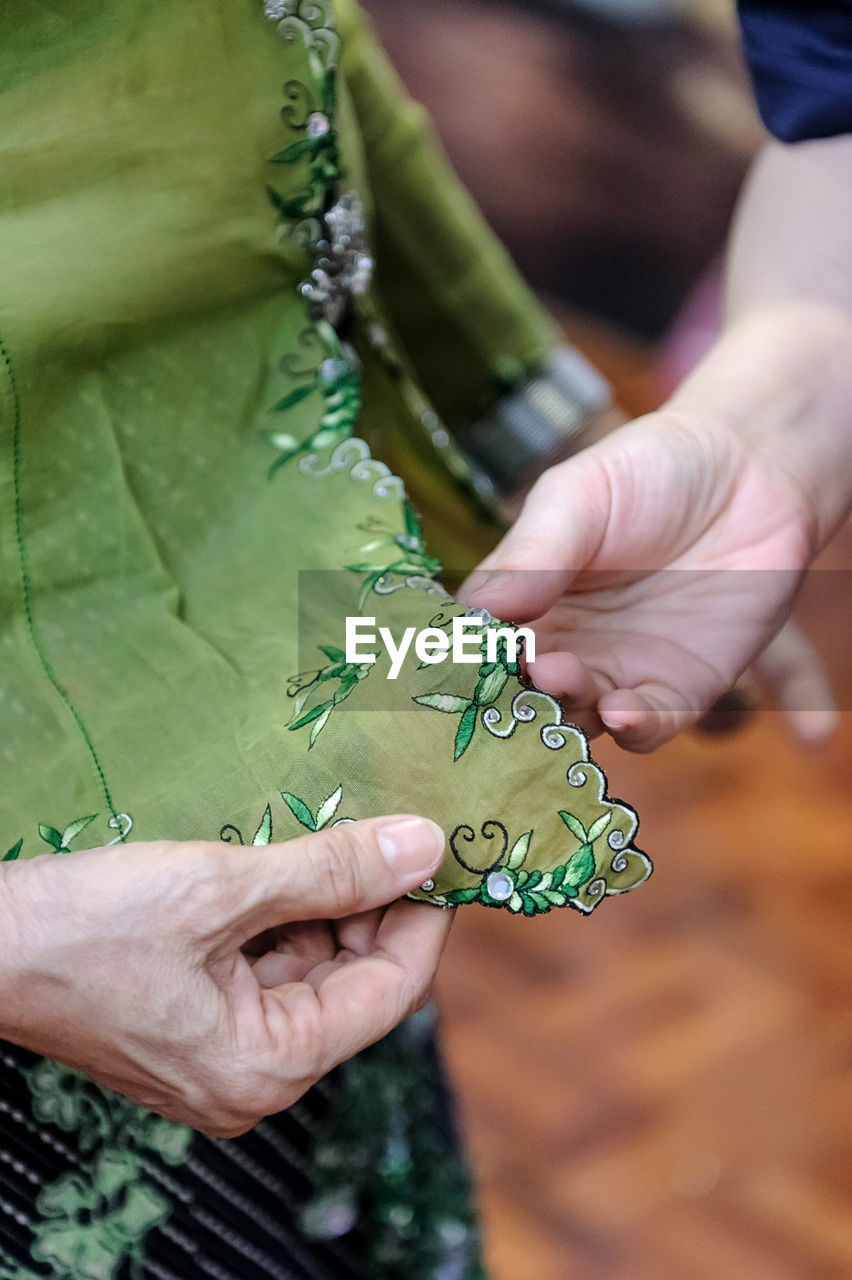 Midsection of women analyzing embroidery on green fabric