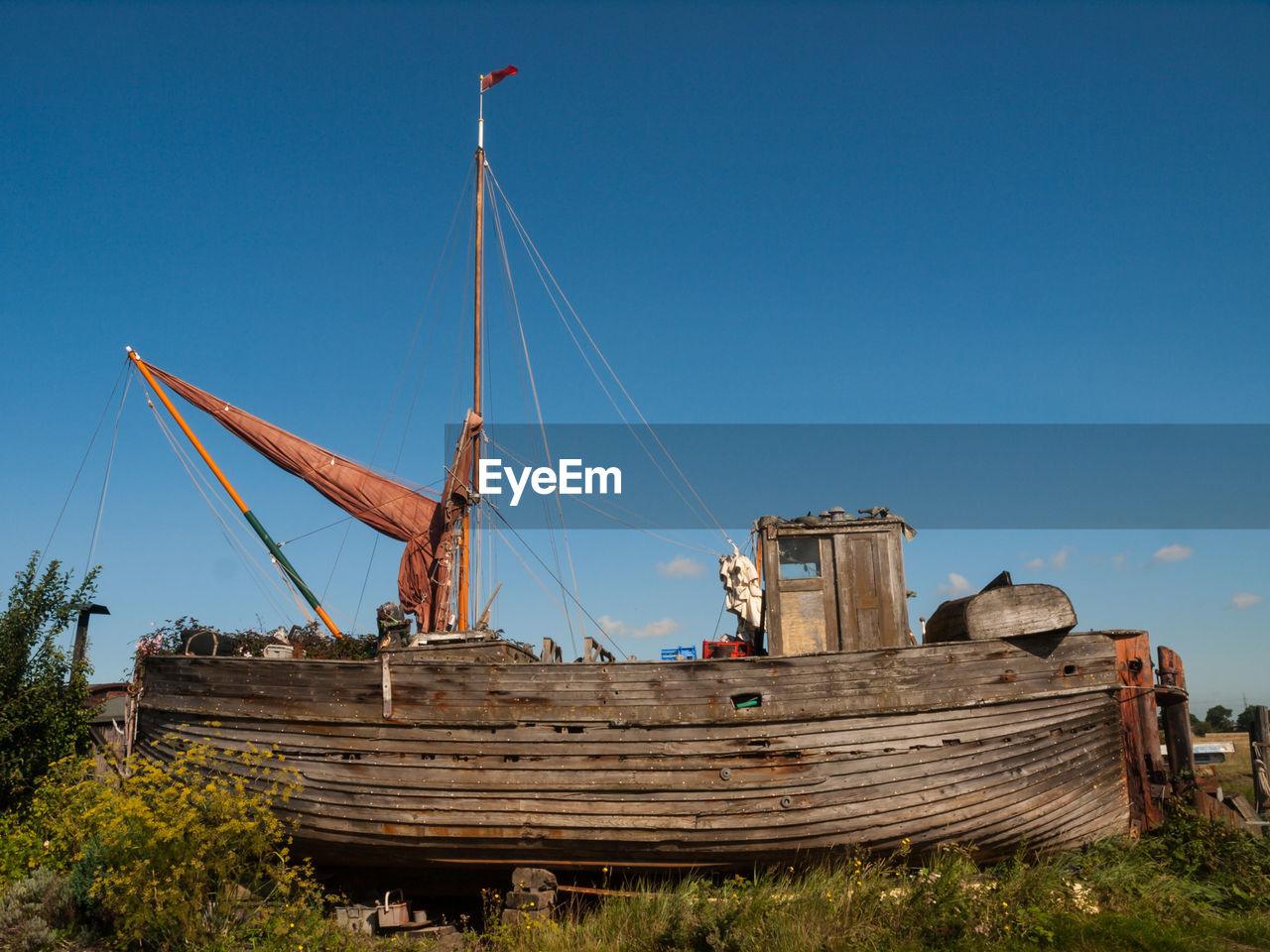 Abandoned boat on field against blue sky