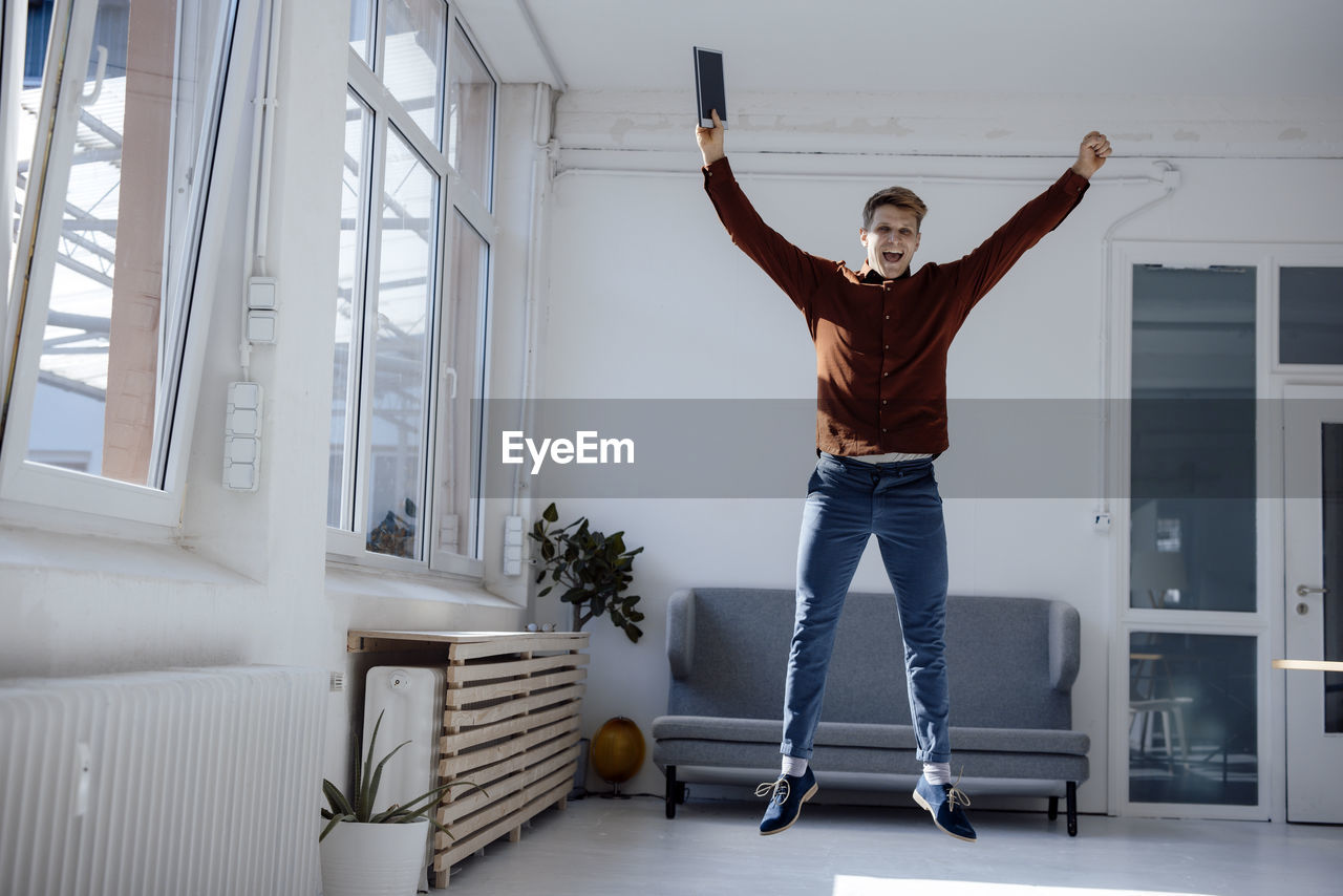 Happy businessman with tablet pc jumping in office