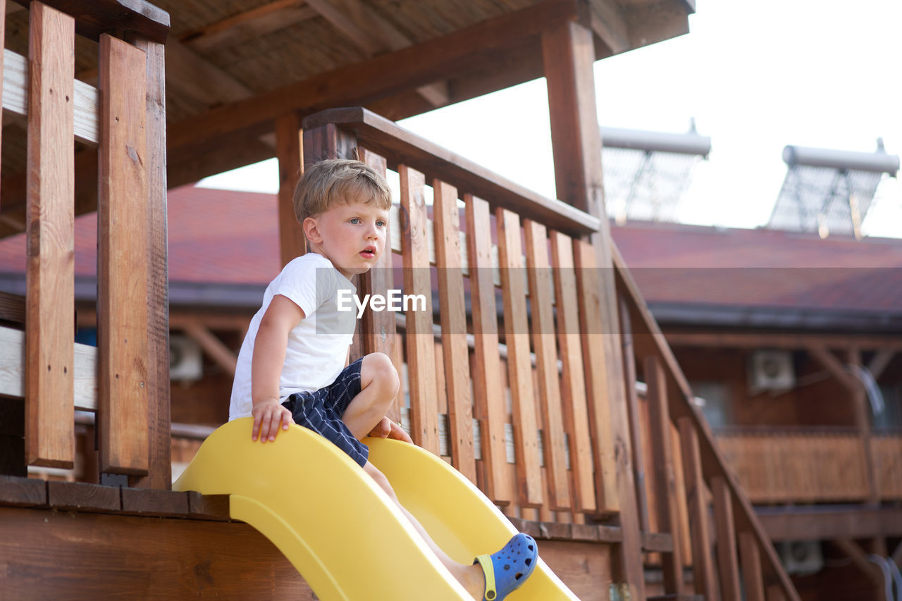 Boy looking away while sitting on slide