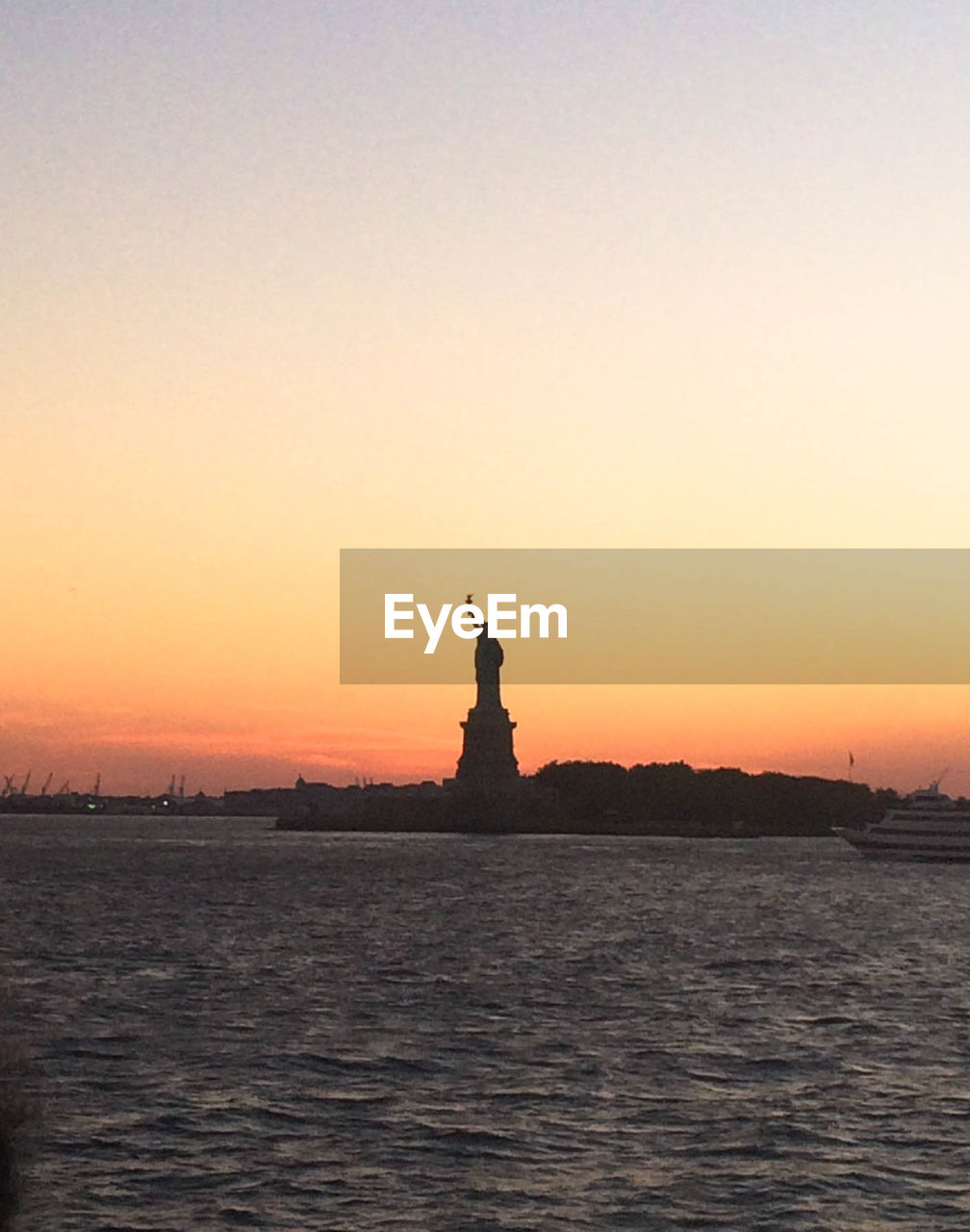 Statue of liberty by sea against sky at dusk