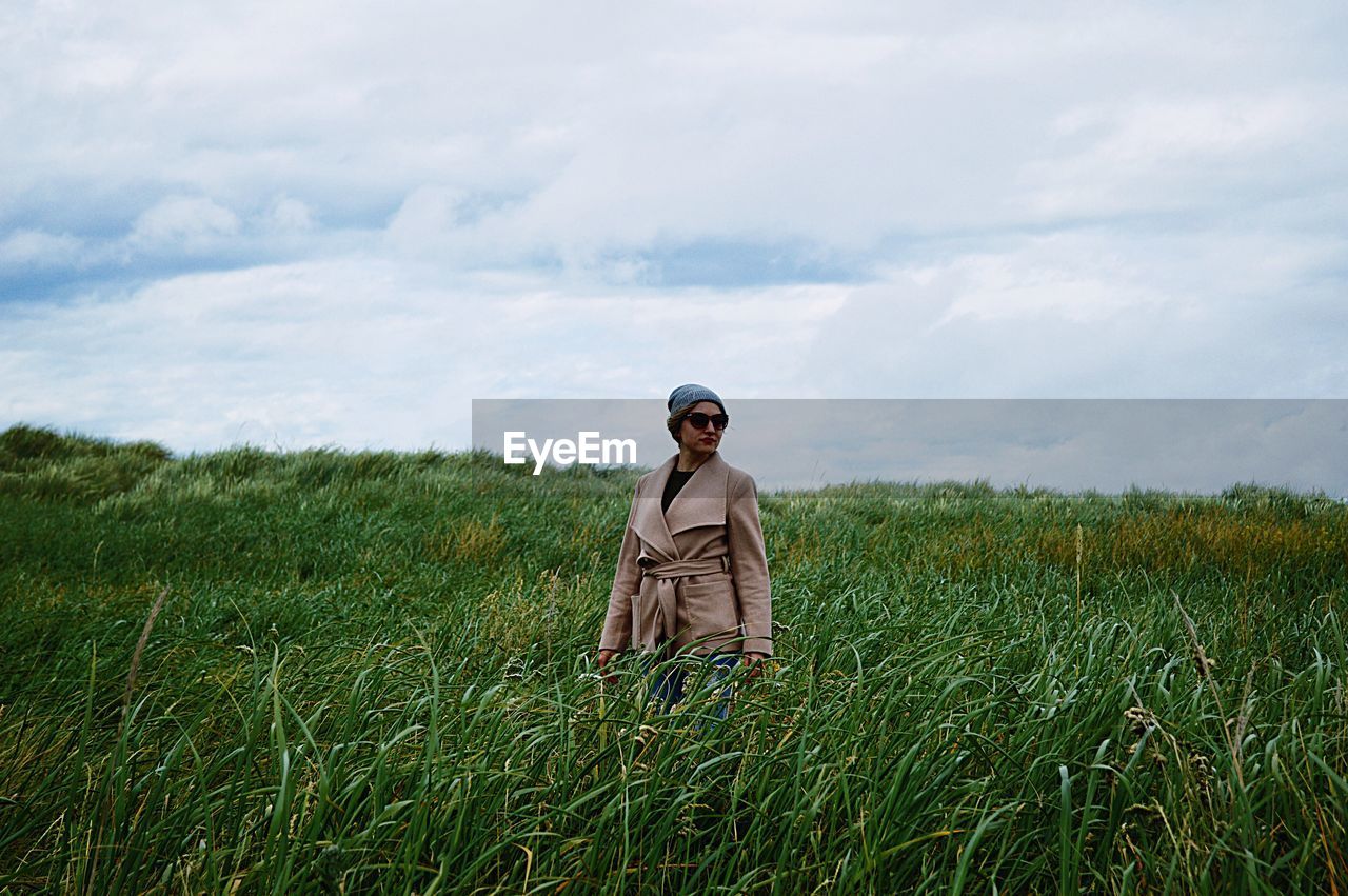 Woman looking away while standing on field against cloudy sky