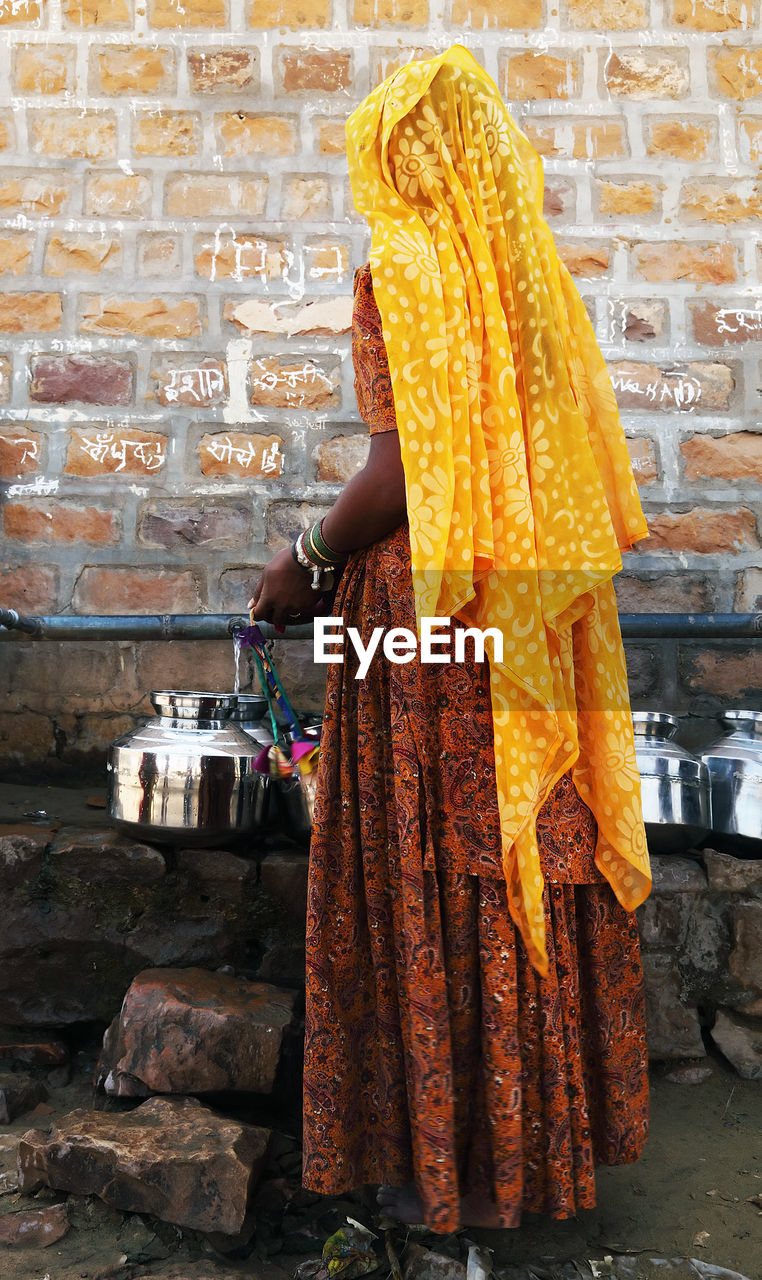 Rear view of woman in traditional clothing filling water in container