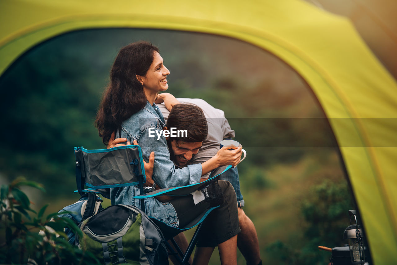 Smiling couple sitting by tent outdoors