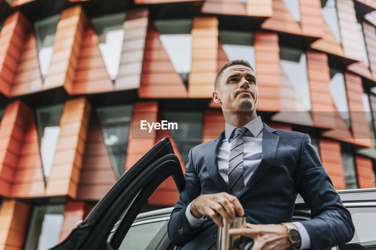 Low angle view of businessman standing near car in front of building