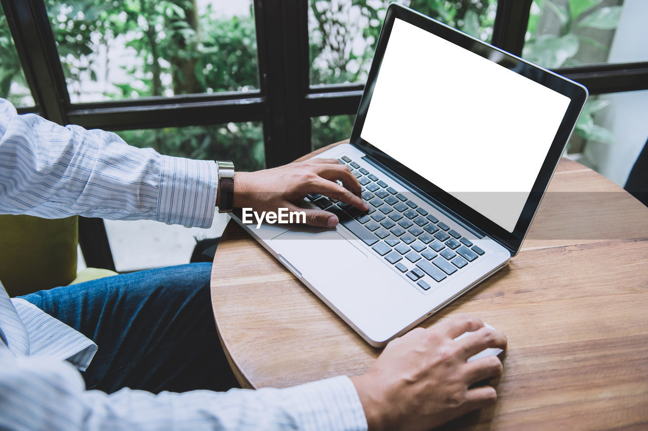 Businessman hands using a laptop with blank screen on desk in the cafe.