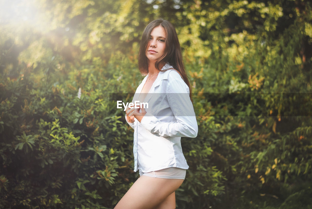 Portrait of beautiful young woman standing against plants