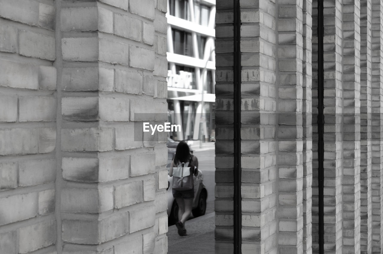 Rear view of woman walking on footpath seen through architectural columns