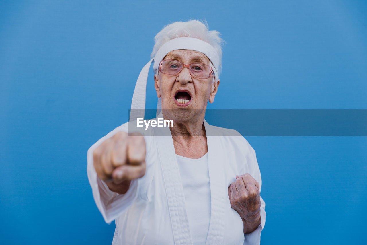 Portrait of senior woman doing karate against blue background