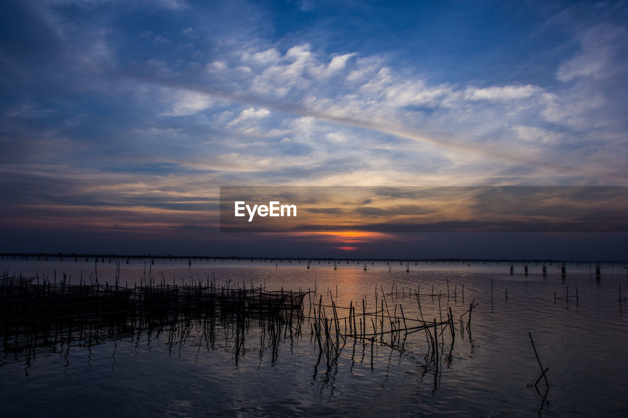 SILHOUETTE WOODEN POSTS IN LAKE AGAINST SKY DURING SUNSET