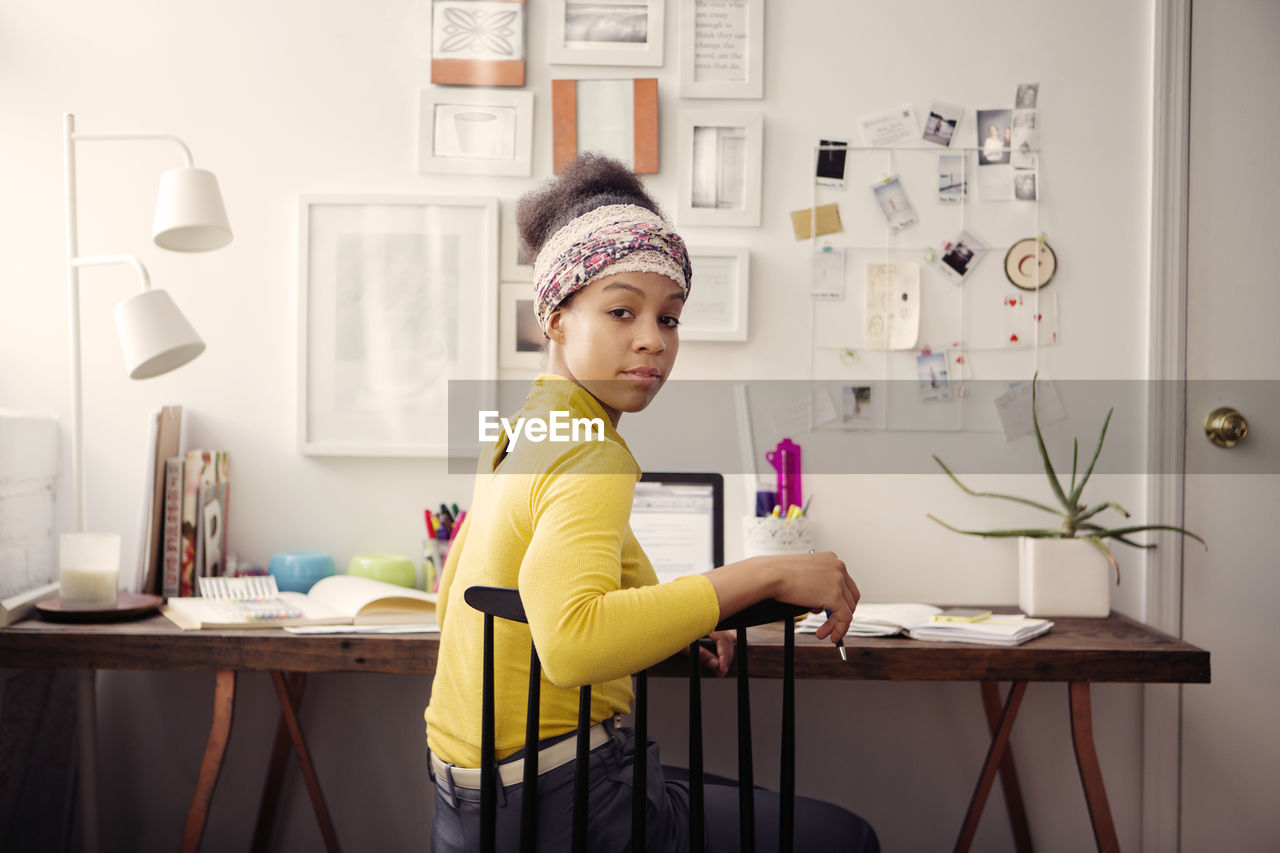 Portrait of woman working on laptop computer at table against papers on wall