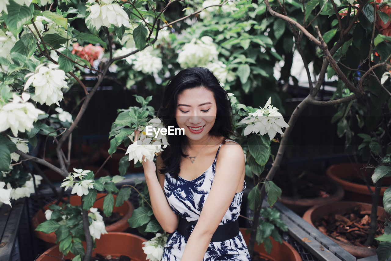 Smiling young woman sitting by flower growing in park