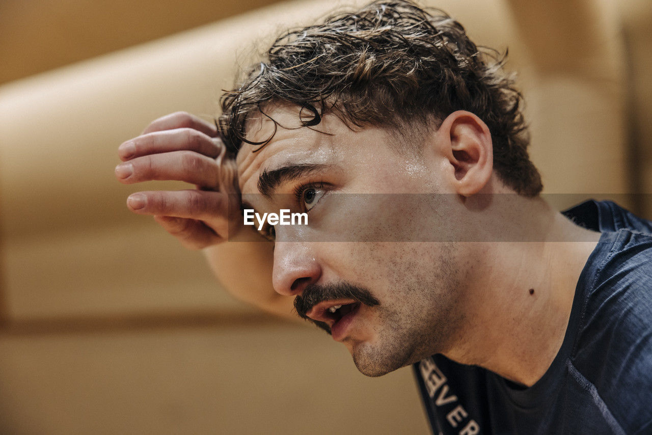 Tired male athlete wiping sweat while contemplating at sports court