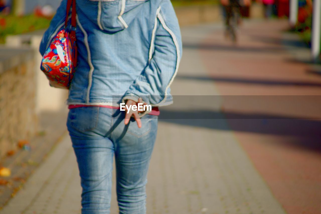 Rear view of woman showing peace sign on road