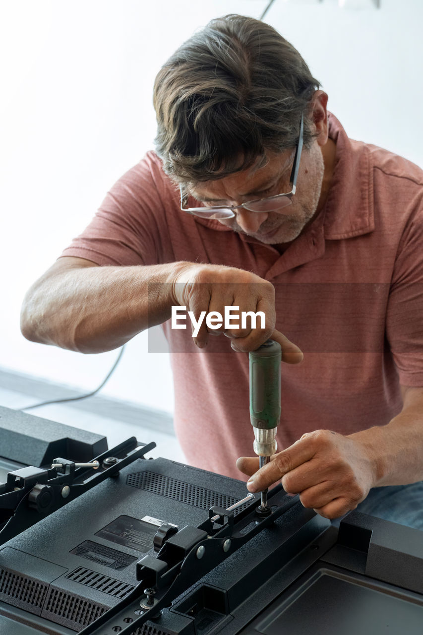 Man installing the wall base for the television, it is a smart tv, adjusting with screwdriver