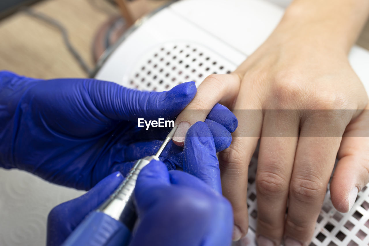 The manicurist cuts the cuticles of the nails with an electric milling machine wearing blue latex