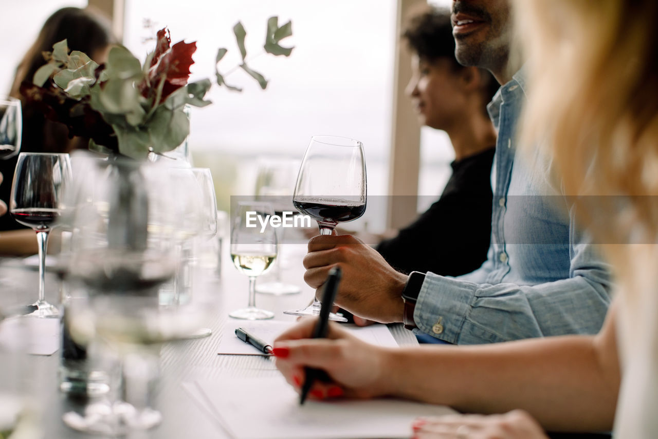 Businessman holding wineglass while sitting with colleagues at table in convention center