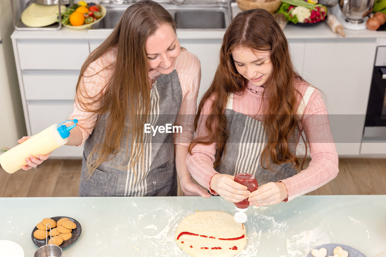 In the kitchen at home, a playful mother and daughter yell while making pizza dough.