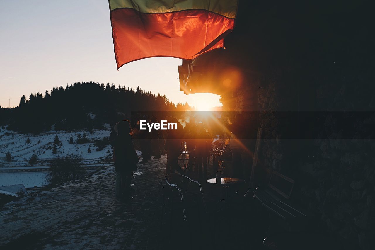 People standing outside house against bright sun during winter