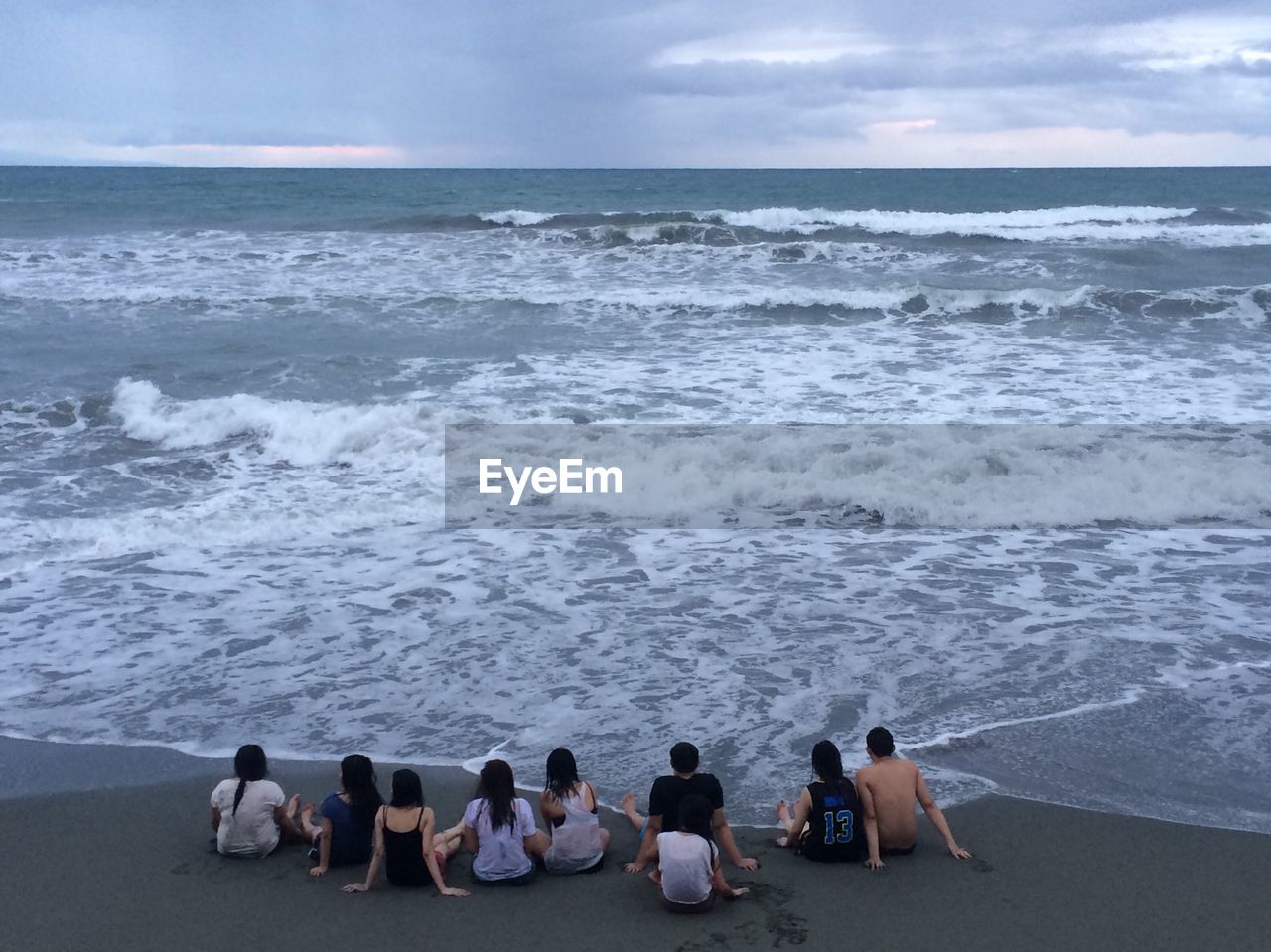 Rear view of friends sitting at beach against sky