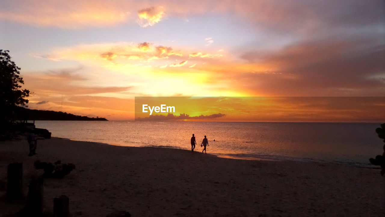 Silhouette of people walking on beach at sunset