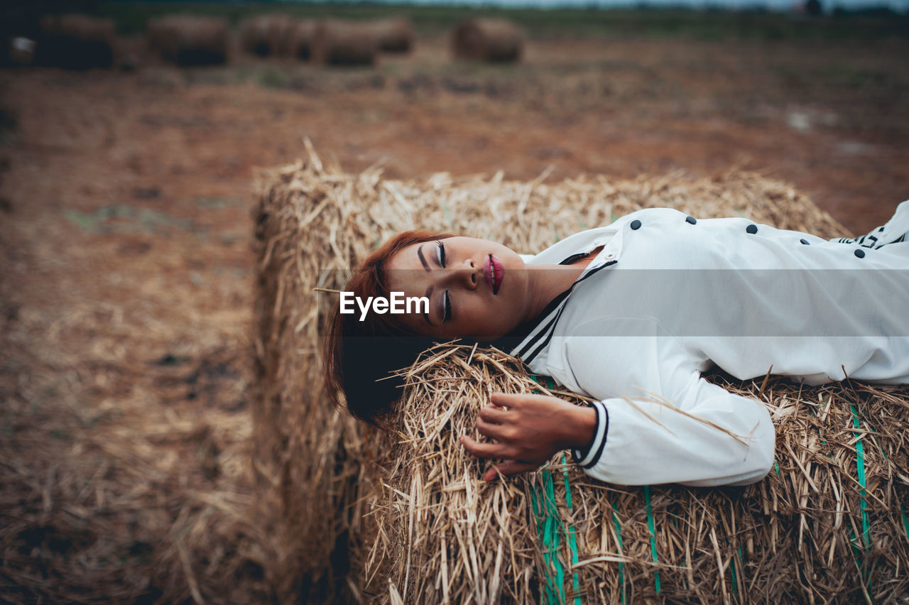 High angle view of young woman lying on hay bale at farm
