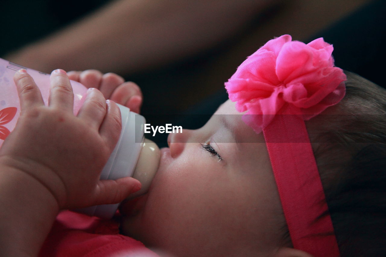 Close-up of baby girl with milk bottle sleeping at home