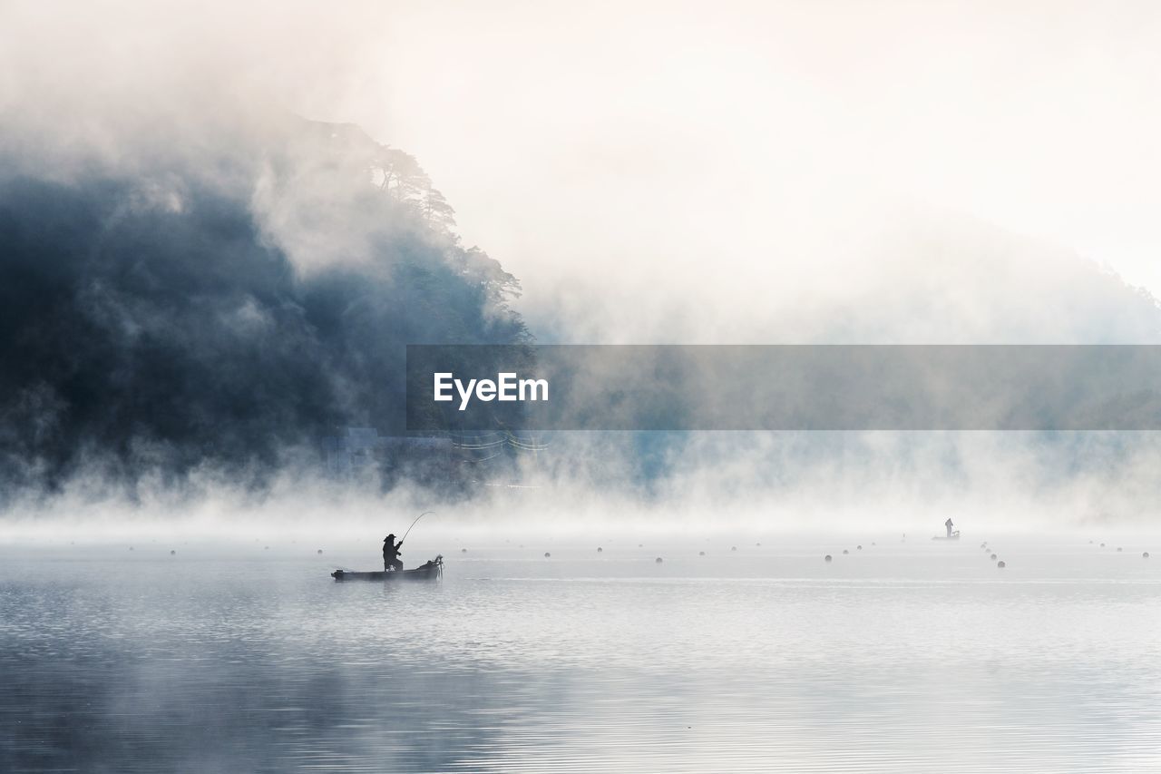 Silhouette fisherman fishing on boat in lake during foggy weather